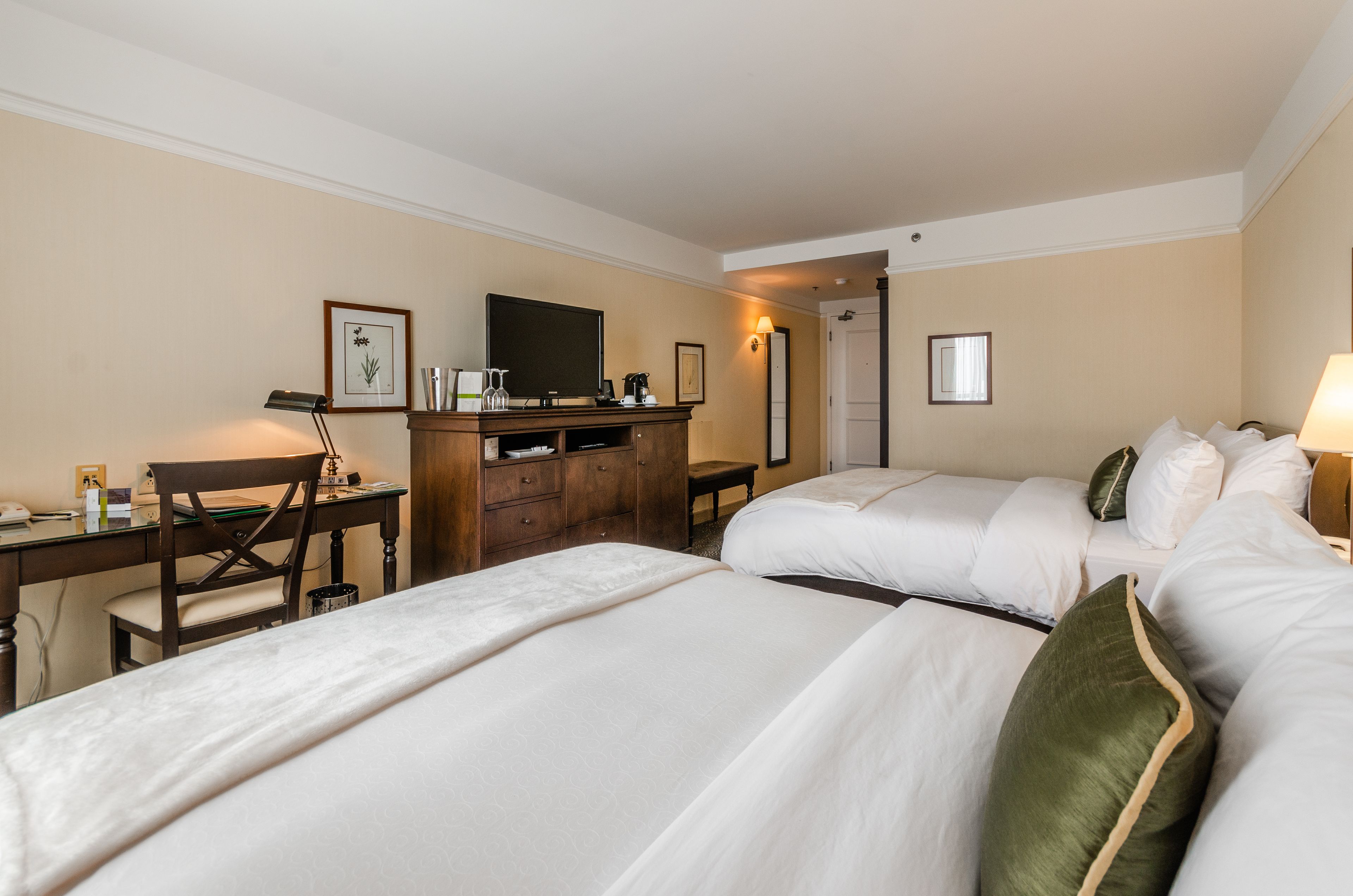 Una habitación de hotel con dos camas, un escritorio, una silla, un aparador y un televisor.