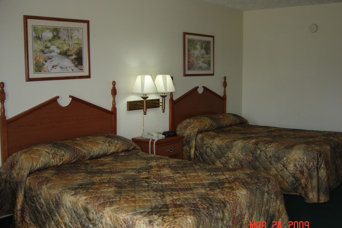 A hotel room with two beds, a nightstand with a lamp, and two framed pictures on the walls.