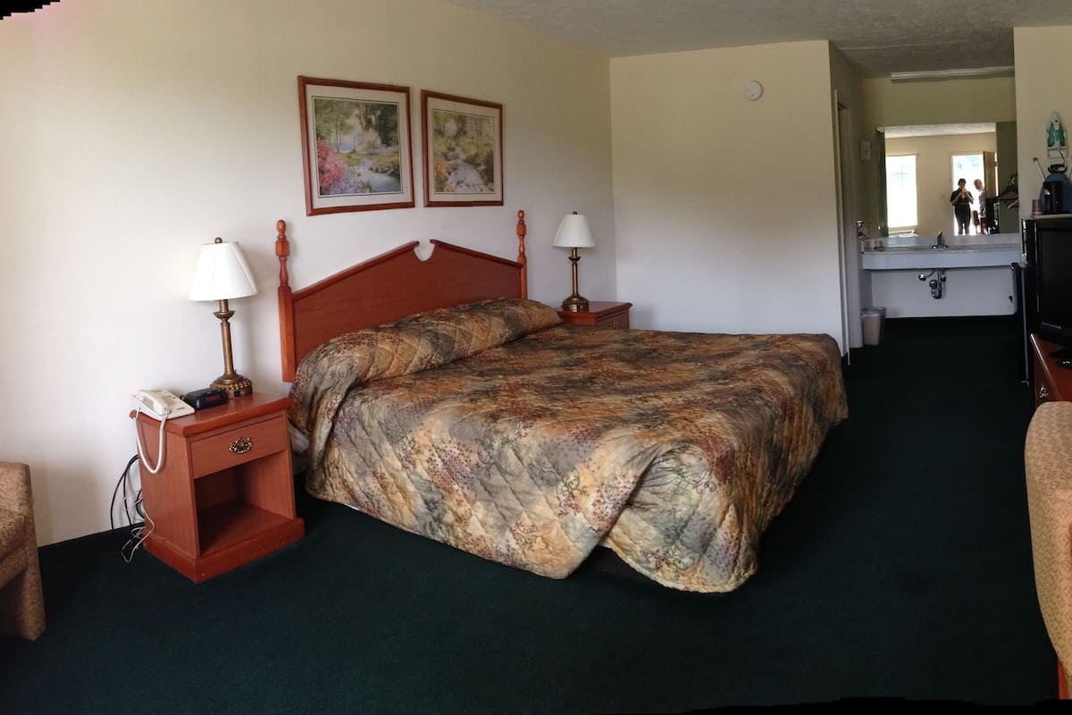 A hotel room with a bed, two bedside tables with lamps, a chair, a television, and a mirror.
