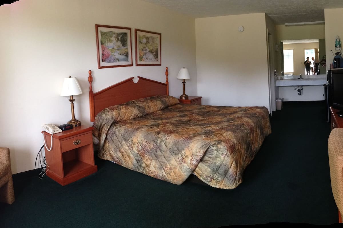 A hotel room with a bed, two bedside tables with lamps, a chair, a television, and a mirror.