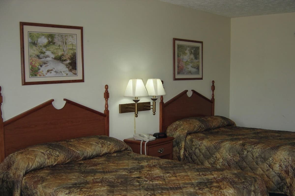 A hotel room with two beds, a nightstand with a lamp, and two framed pictures on the wall.