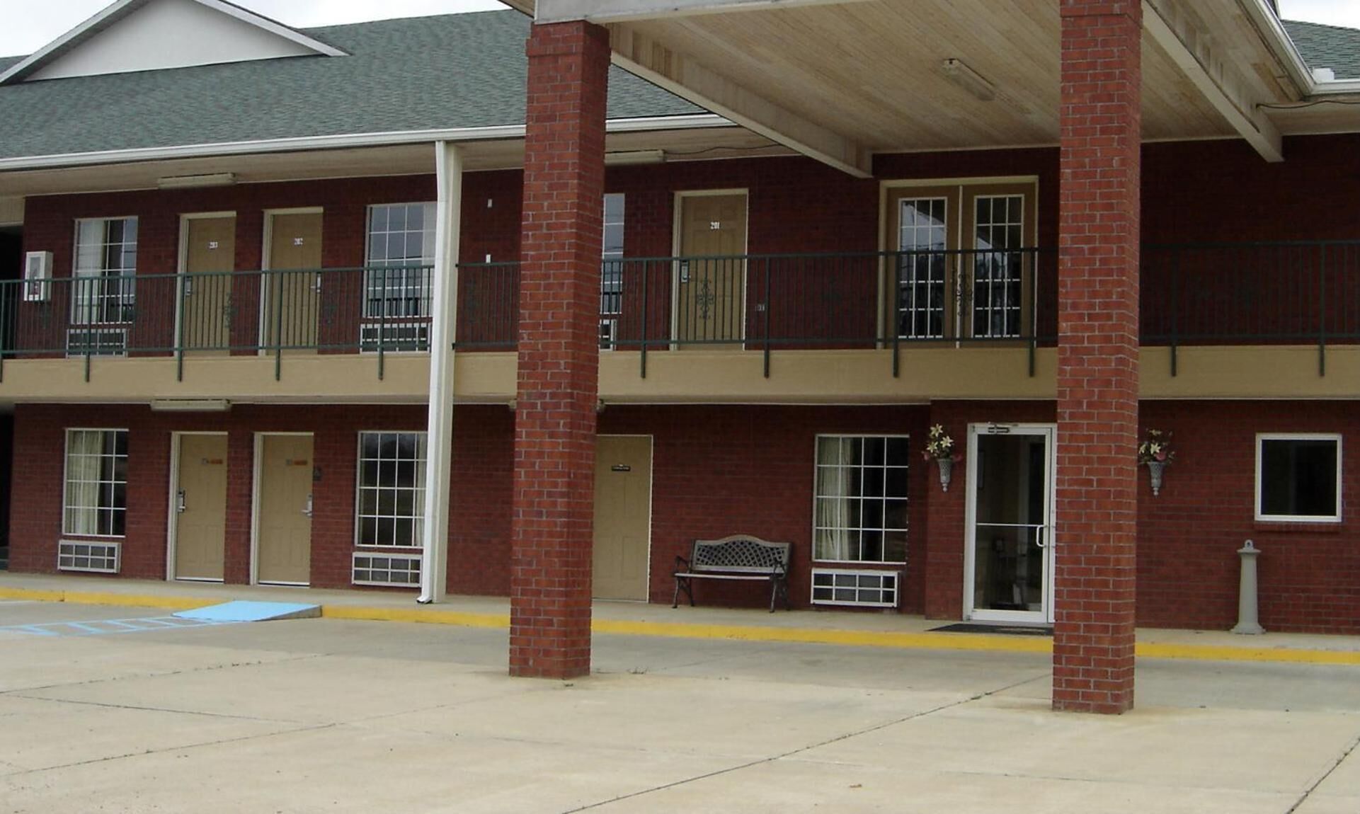 A two-story building with a flat roof, brick facade, and a covered entrance area with a bench.
