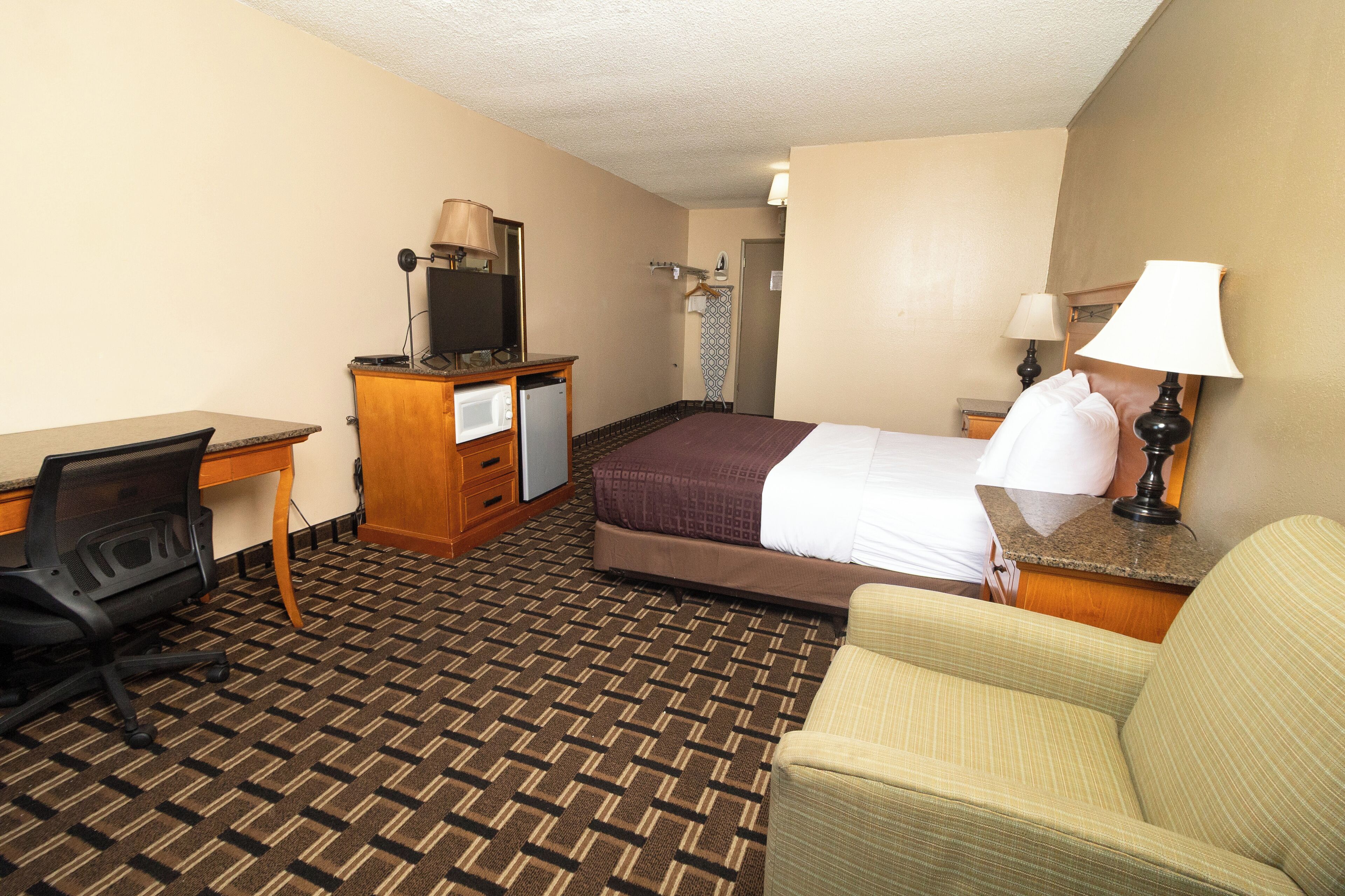 A hotel room with a bed, a desk with a computer, a chair, a TV, and a lamp.