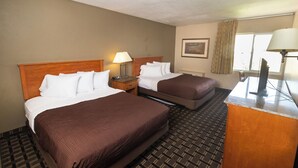 A hotel room with two beds, a desk, a lamp, a painting, and a window with curtains.