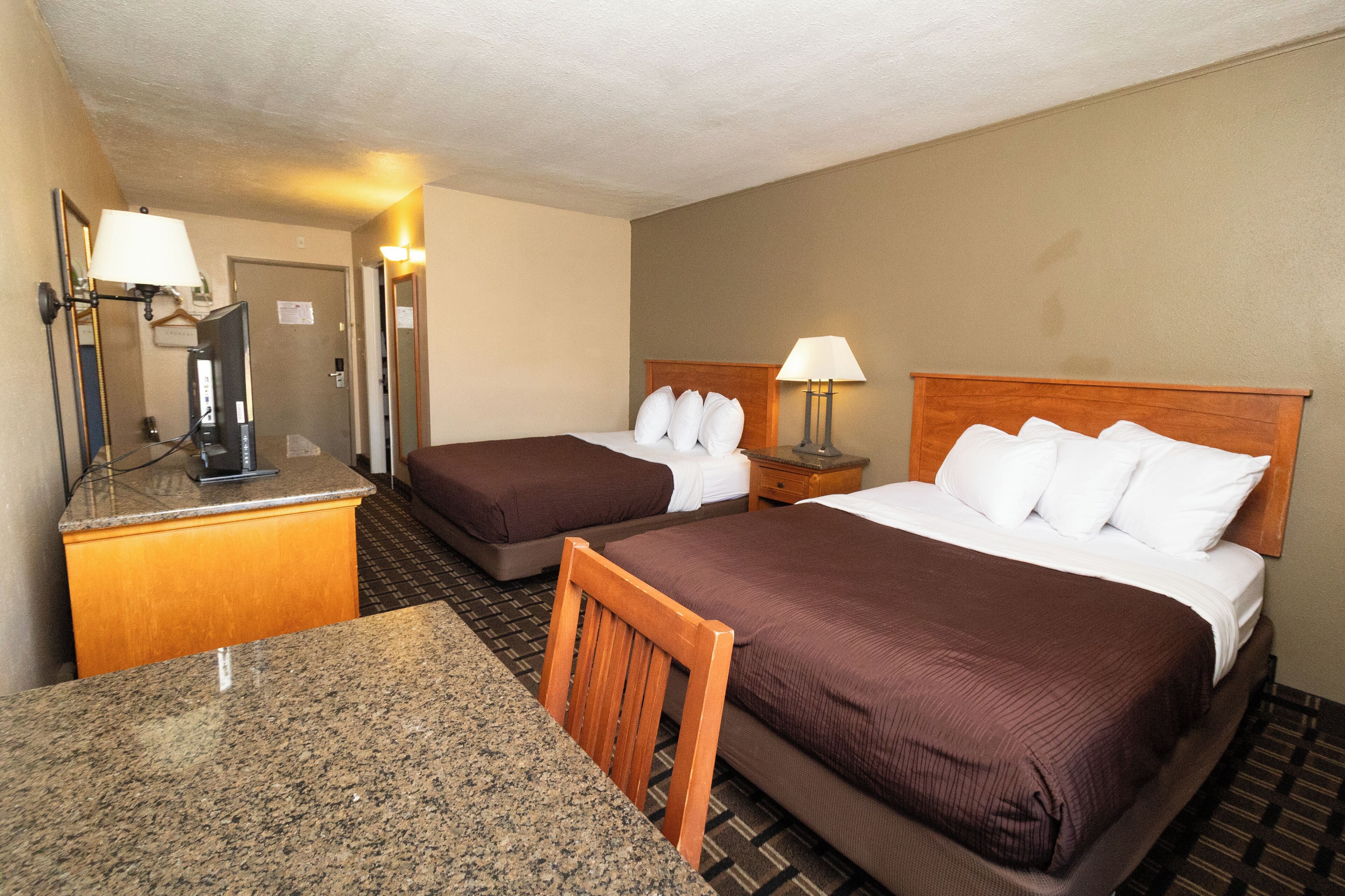 A hotel room with two beds, a desk, and a mirror.