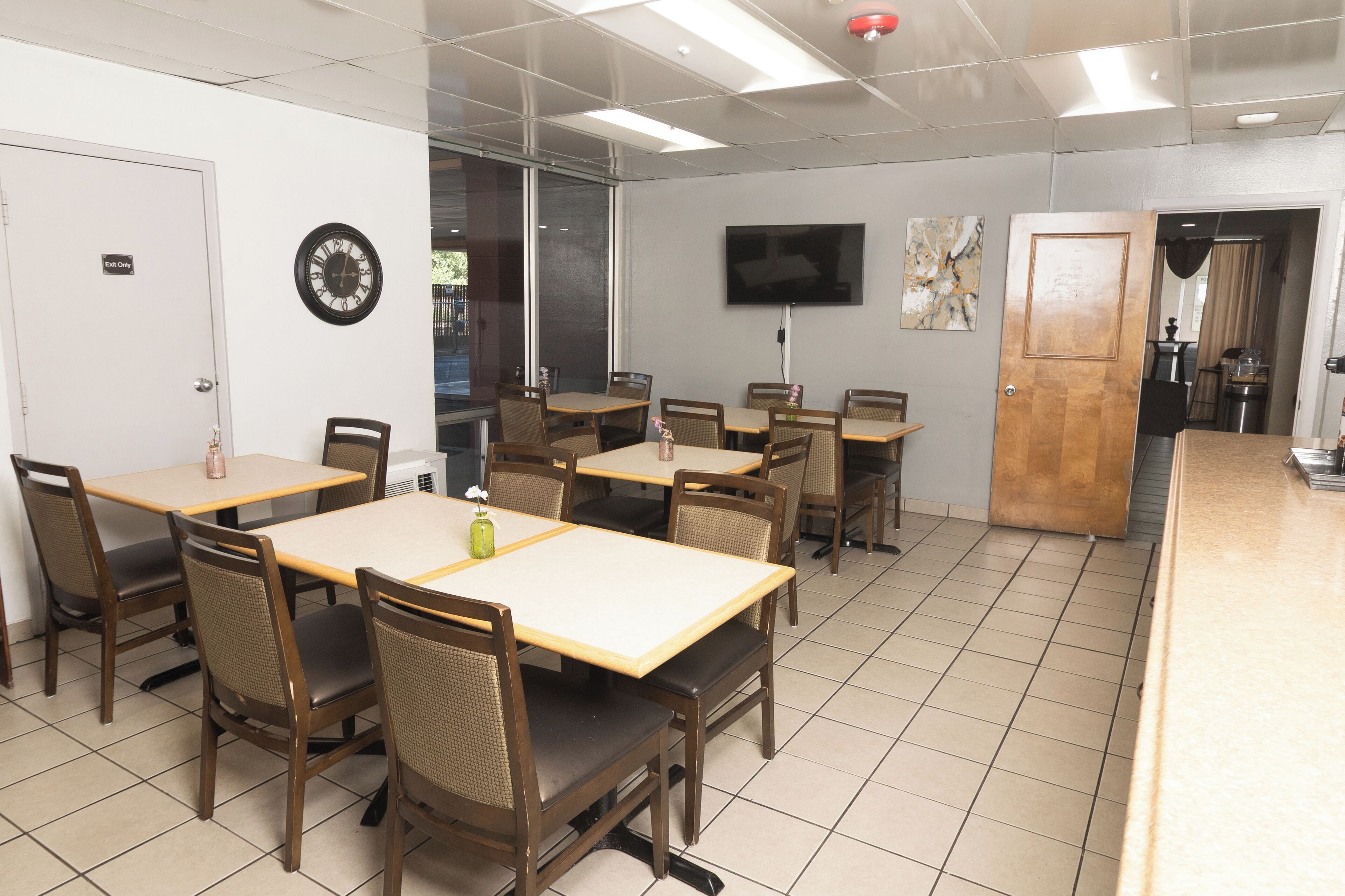 A conference room with multiple tables and chairs, a clock, a TV, and a door labeled "Exit Only".