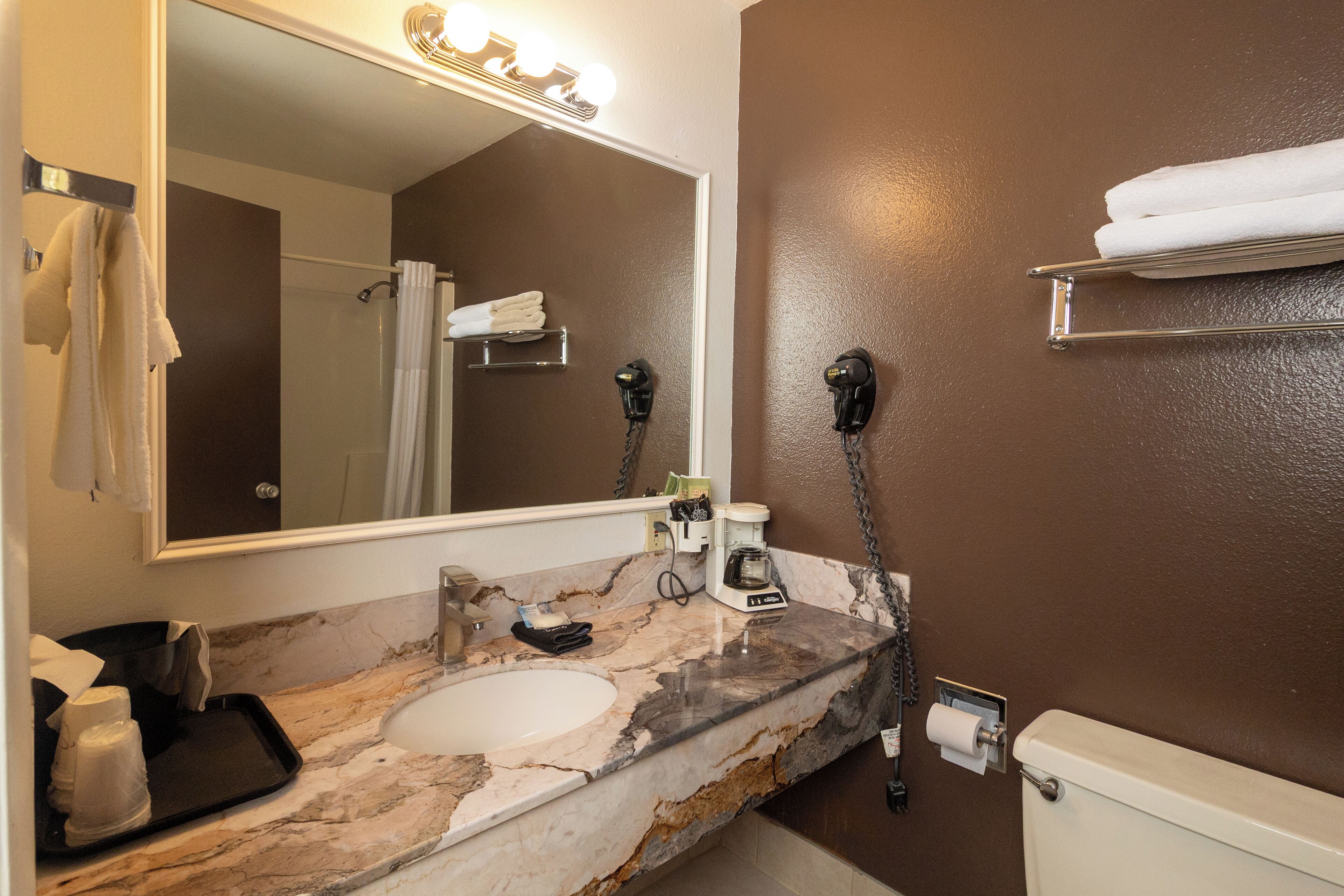 A bathroom with a marble sink, a mirror with lights, a hairdryer, and a towel rack.