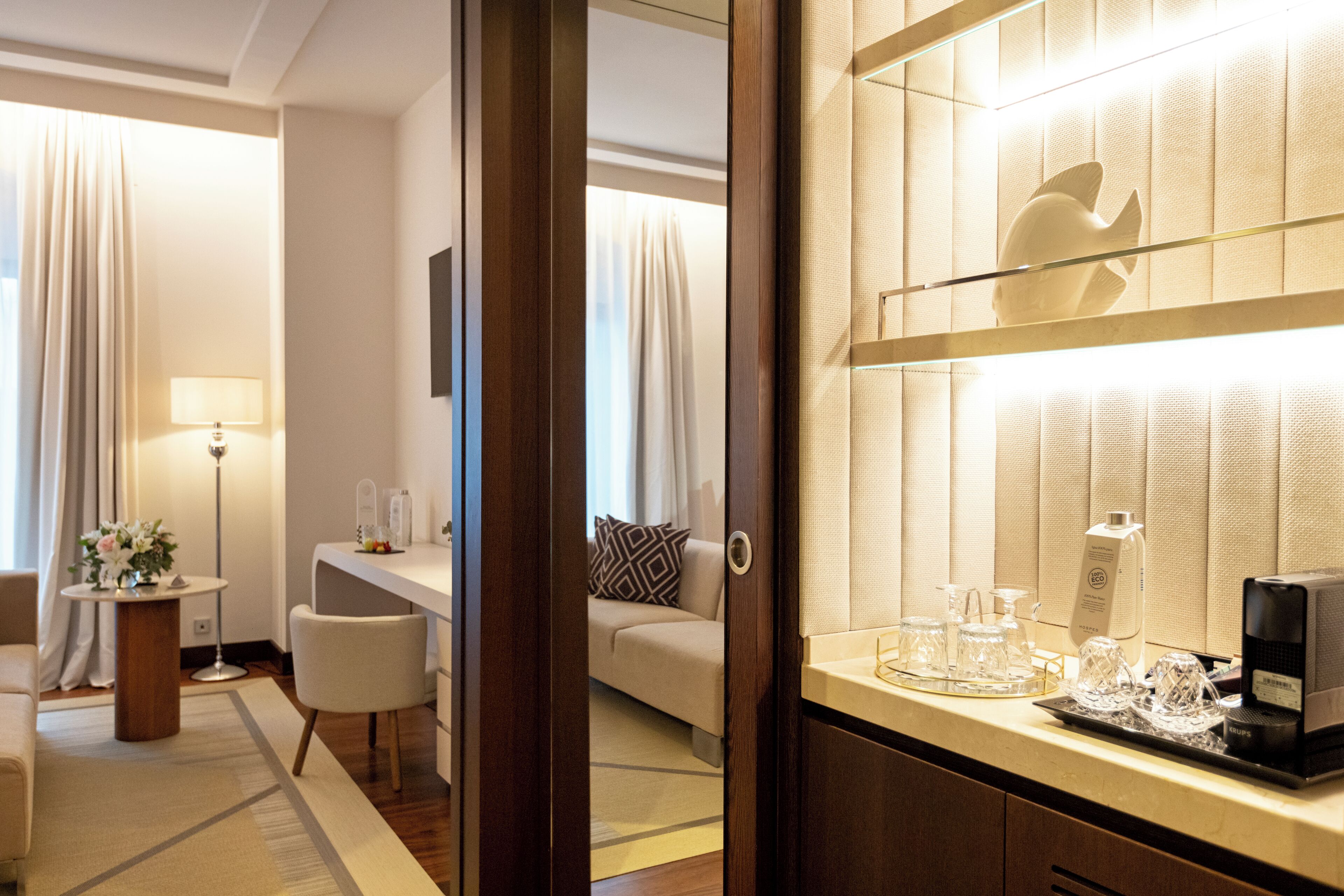 Habitación de hotel con cama, escritorio, silla, cafetera y bandeja con vasos y una botella.