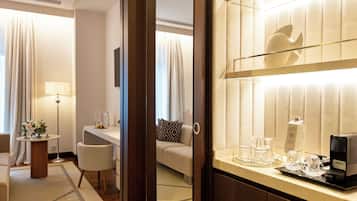 Habitación de hotel con cama, escritorio, silla, cafetera y bandeja con vasos y una botella.