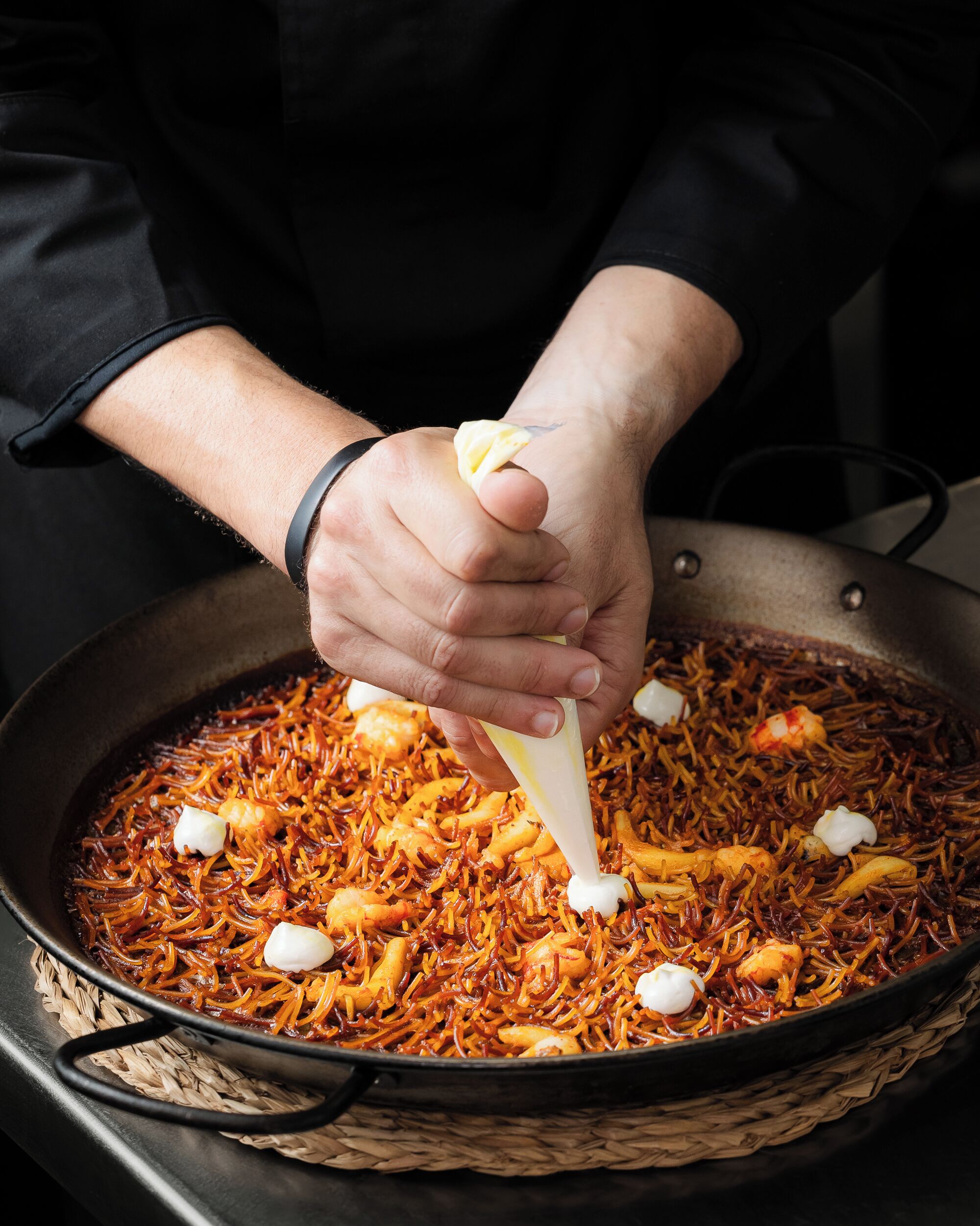 Una persona preparando un plato en una sartén grande.
