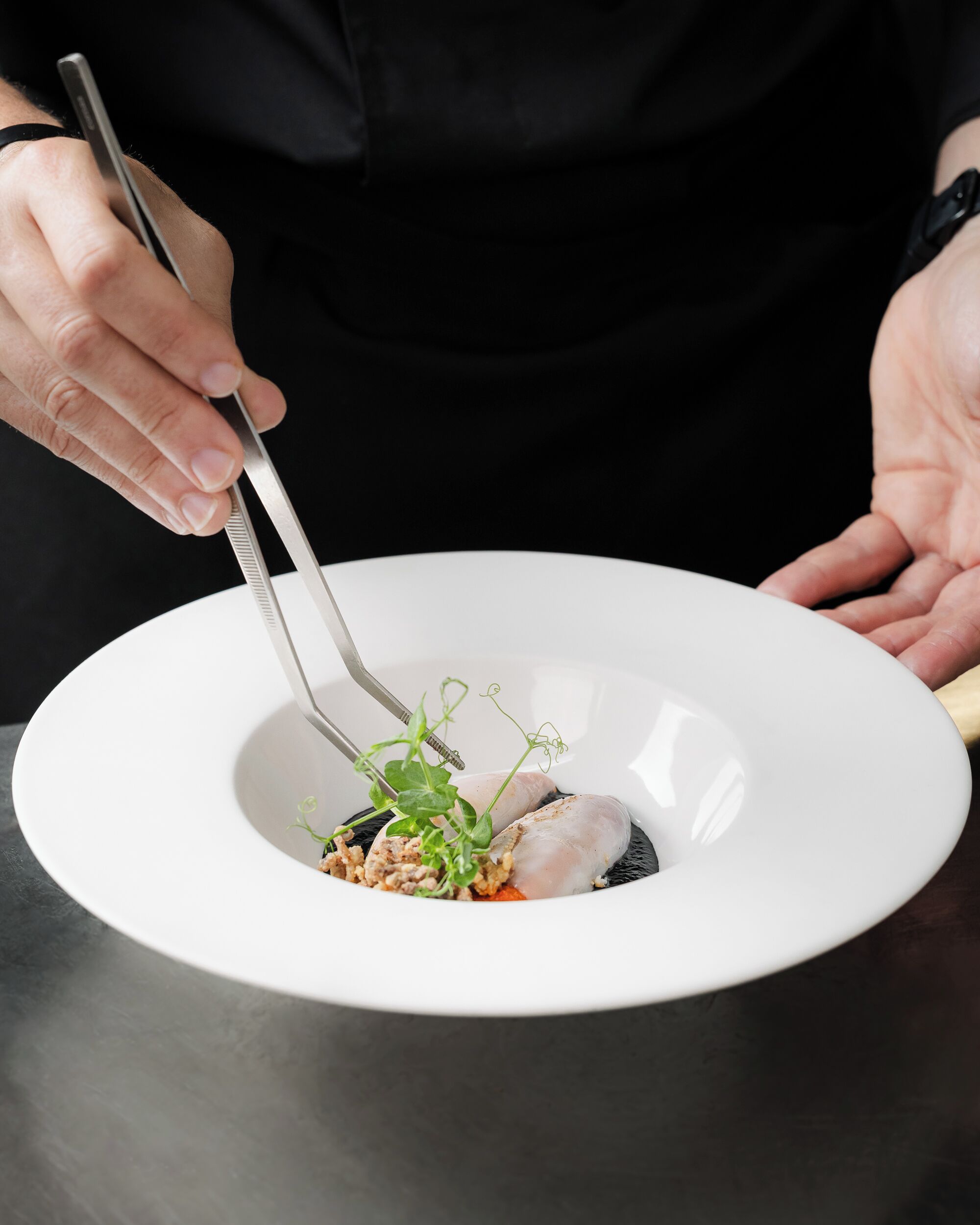 Una persona sosteniendo un tenedor sobre un plato blanco con un agujero central, que contiene un alimento y algo de verdura.