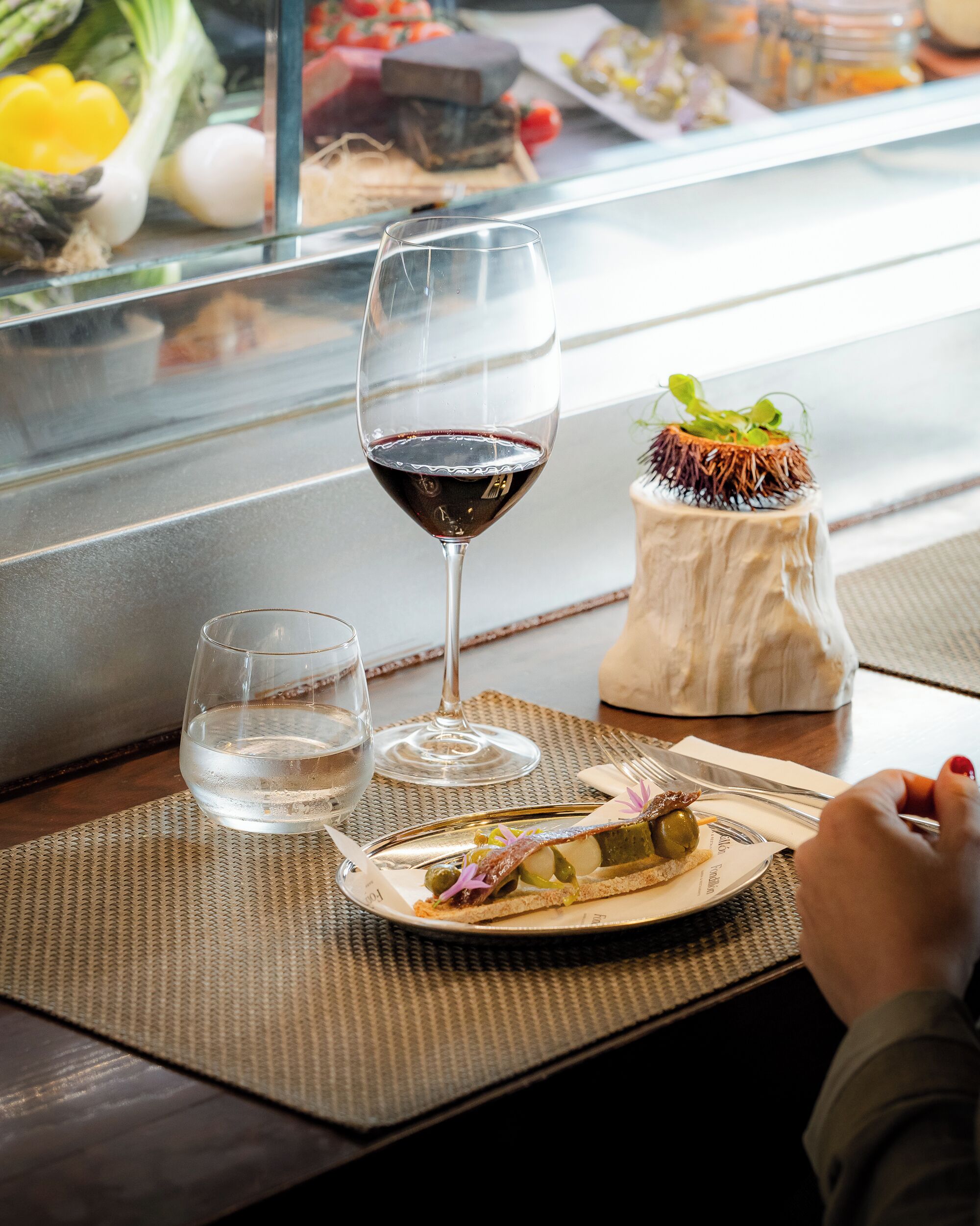 Una mesa de comedor con un plato de comida, dos vasos de agua y una copa de vino tinto.
