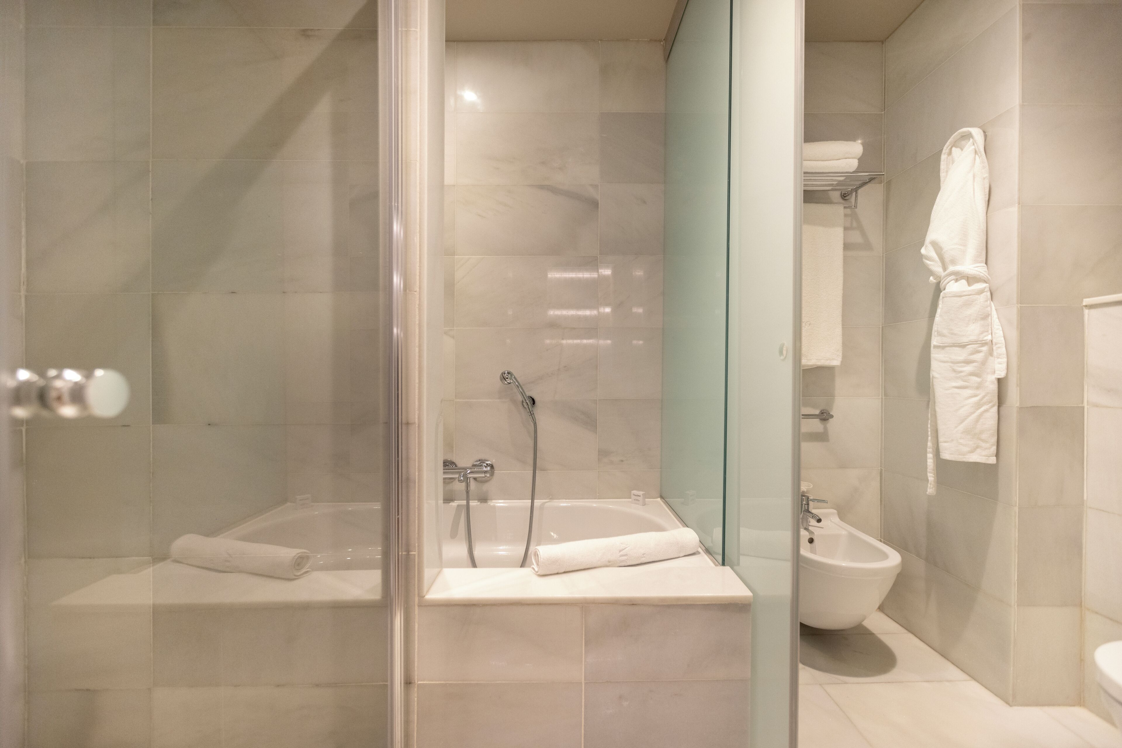 Een moderne badkamer met een douchecabine, een bad, een toiletbril en een witte handdoek op een plank.