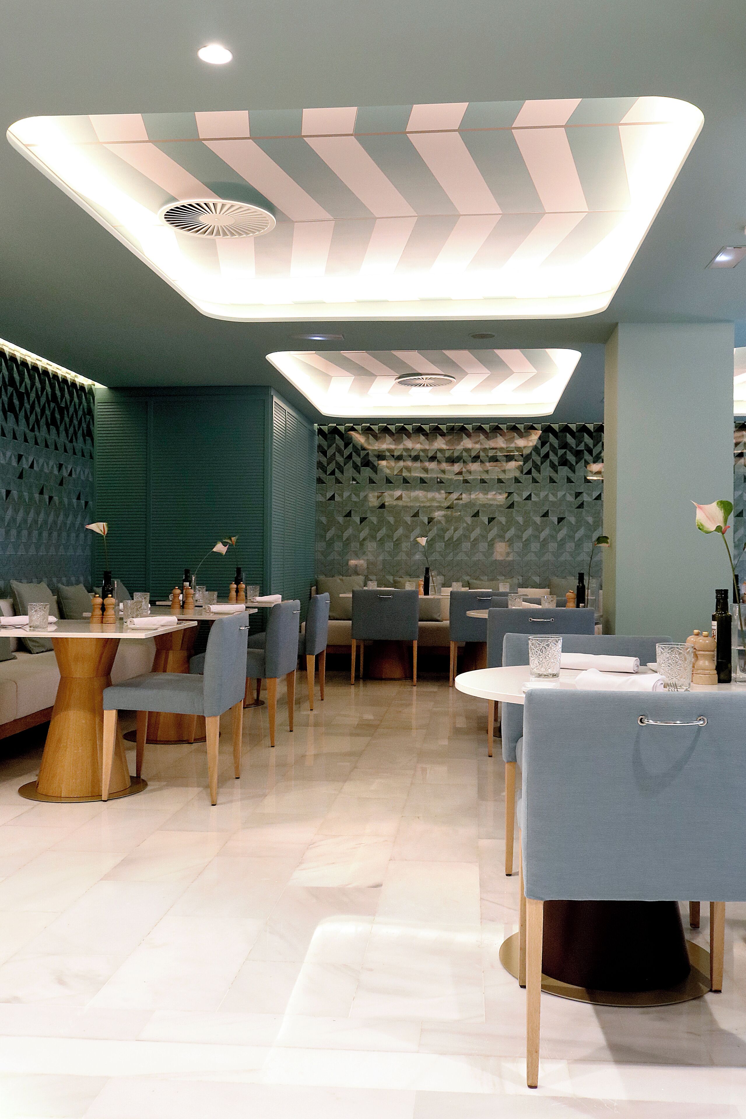 A modern restaurant interior with a geometric ceiling design, cushioned seating, and a clean, tiled floor.