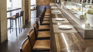 A long dining table with chairs, a glass display case with food items, and a wall with abstract art.