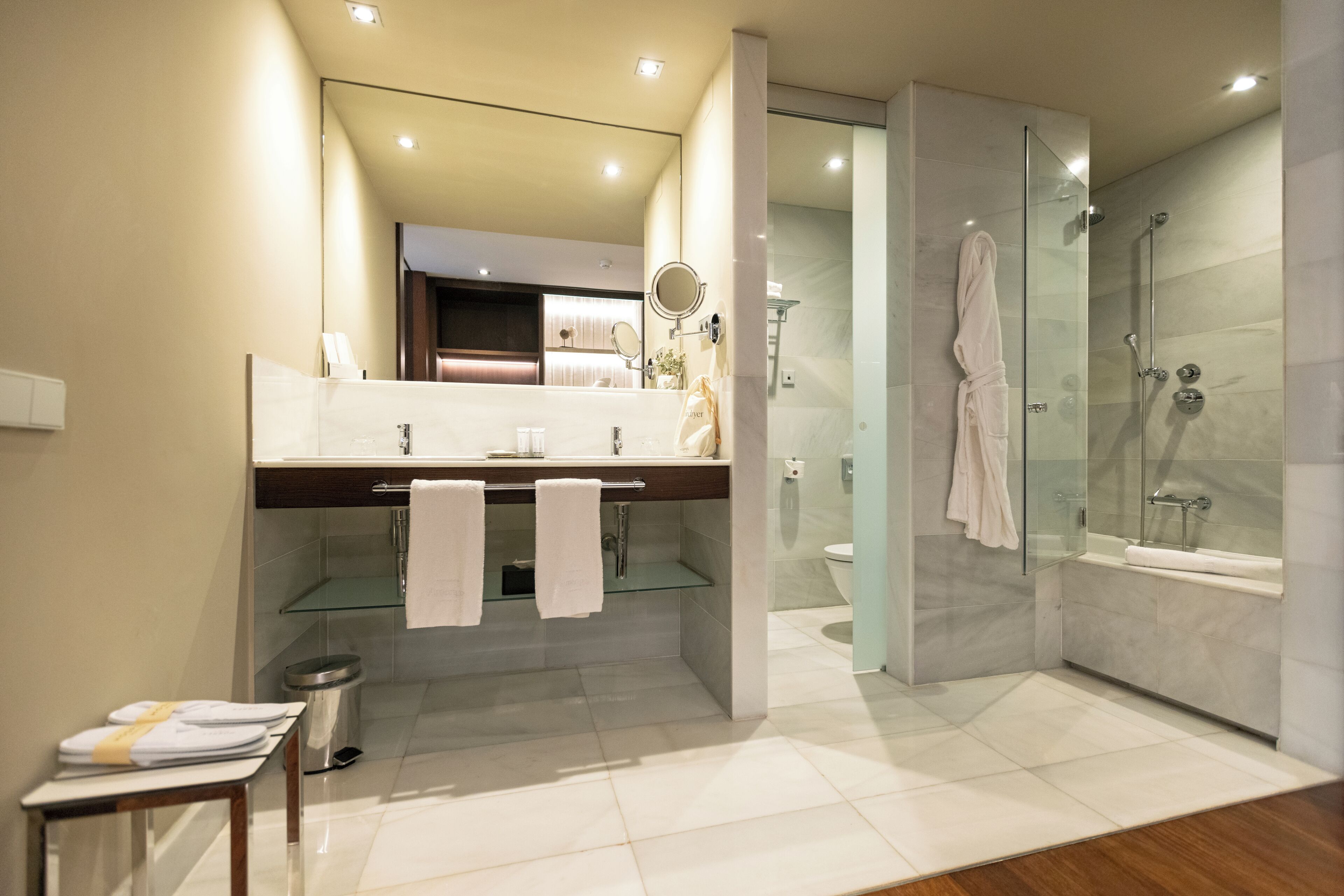 Un baño moderno con ducha de vidrio, tocador con espejo y un inodoro visible al fondo.