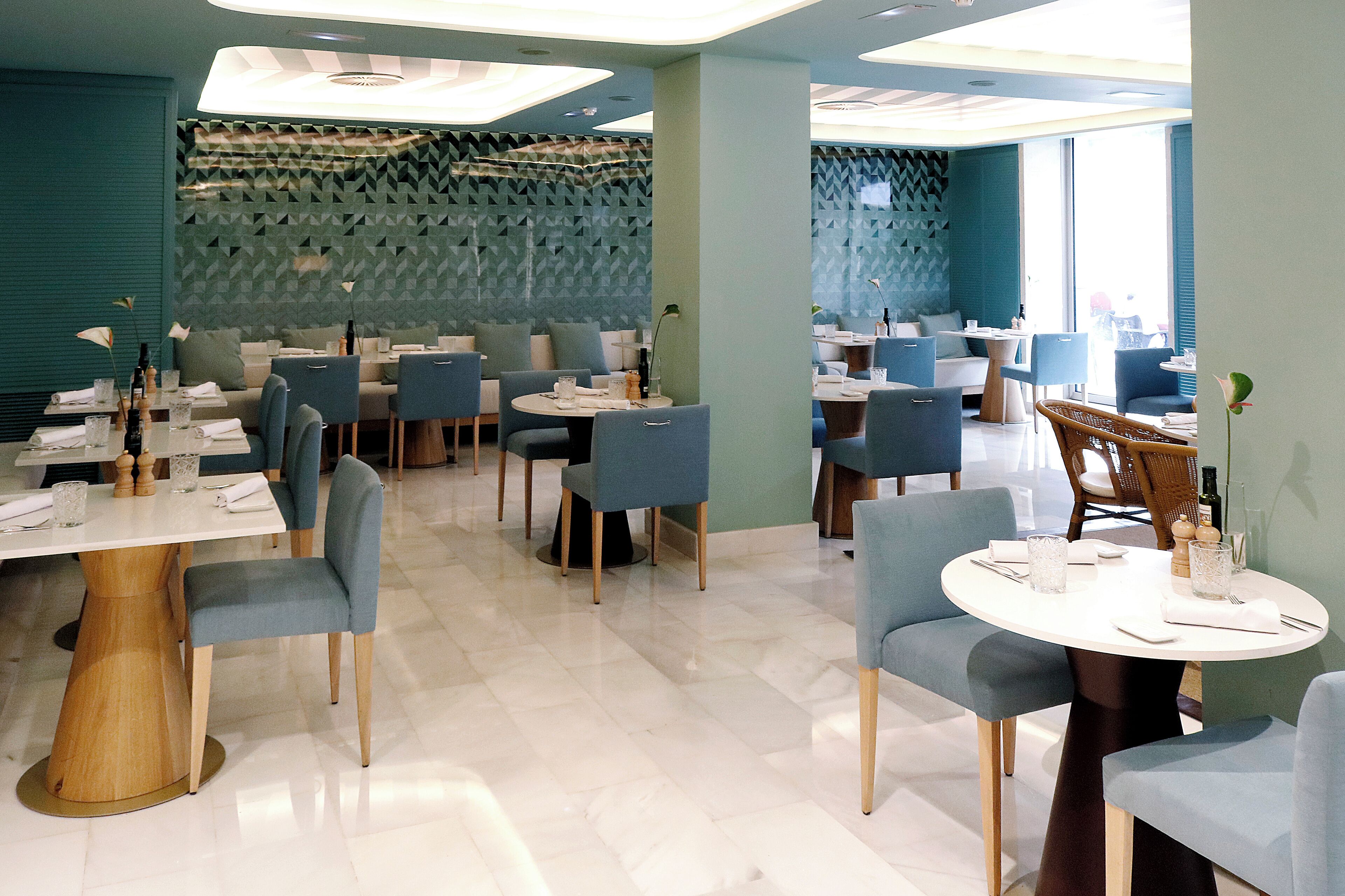 Un restaurante moderno con varias zonas de comedor, cada una con mesas redondas y sillas azules.