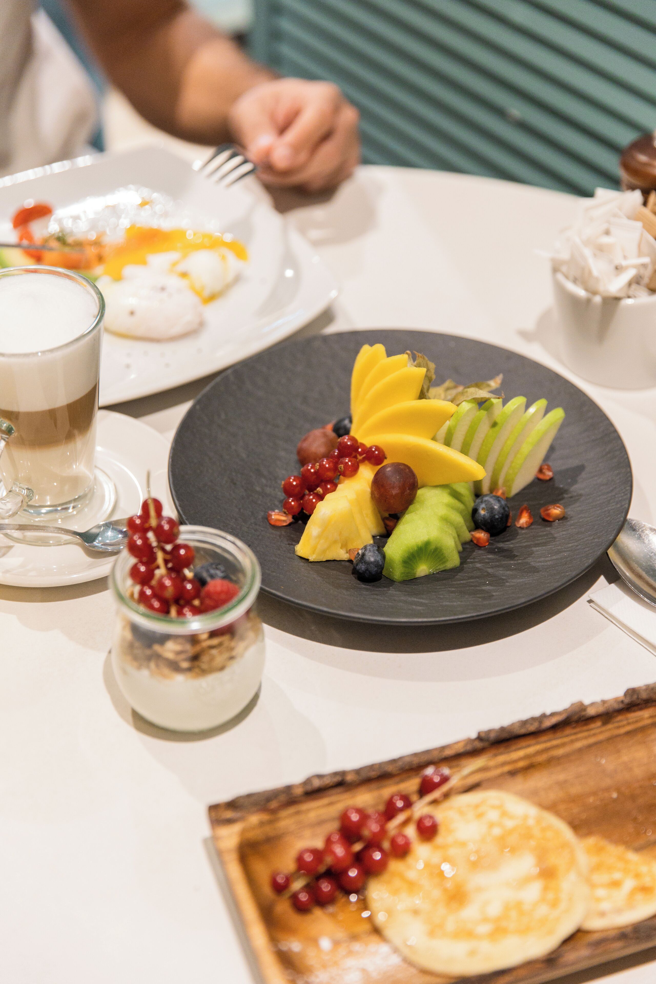 A dining table with plates of food, a glass of a beverage, and a small jar of berries.