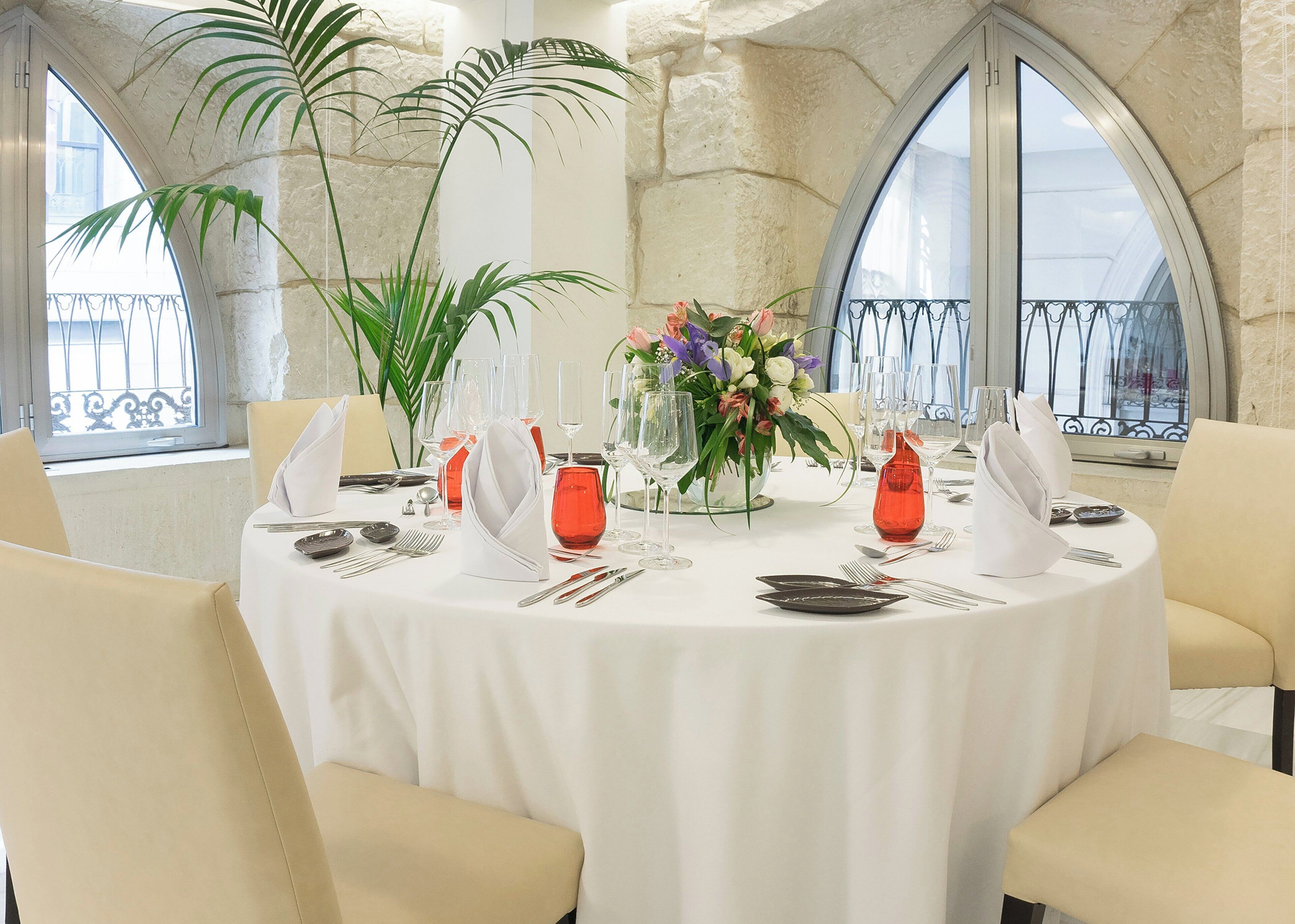 Mesa redonda para seis personas, con mantel blanco, copas de vino tinto y un centro de mesa floral.