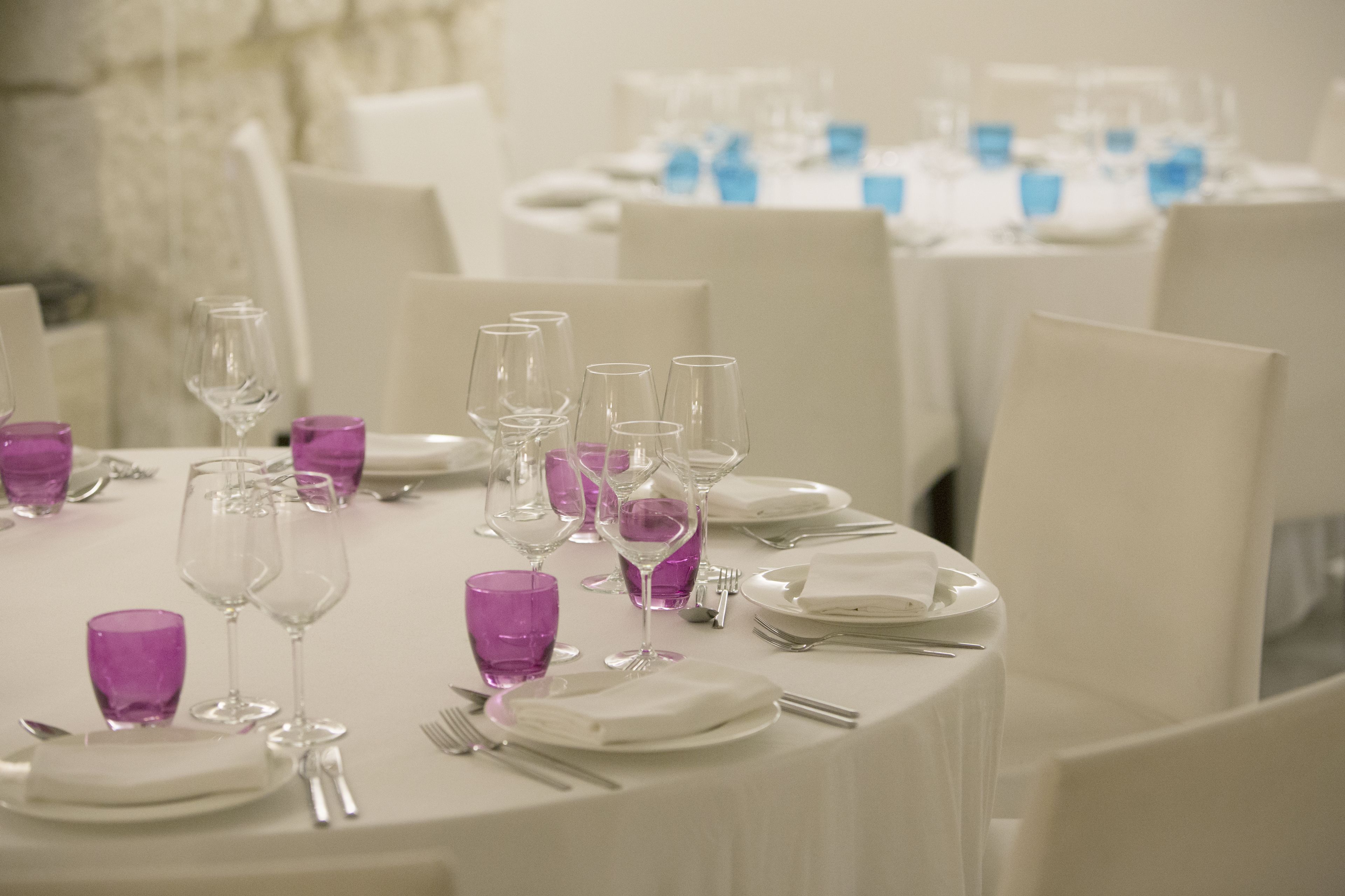 A dining table set with white plates, silverware, and purple glassware, surrounded by white chairs in a formal dining setting.
