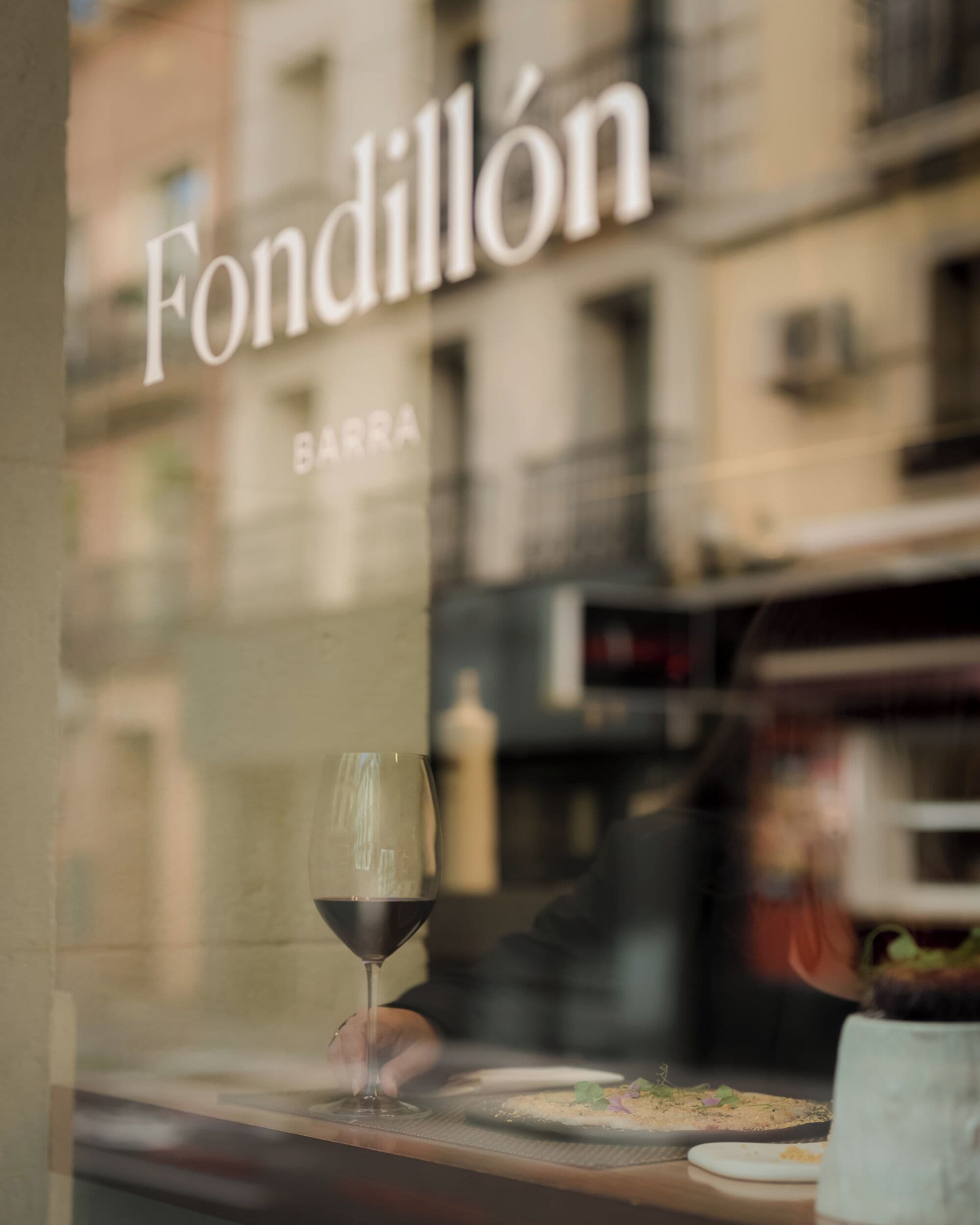 Une fenêtre avec un verre de vin et une assiette de nourriture, sur laquelle on peut lire le nom « Fondillón ».