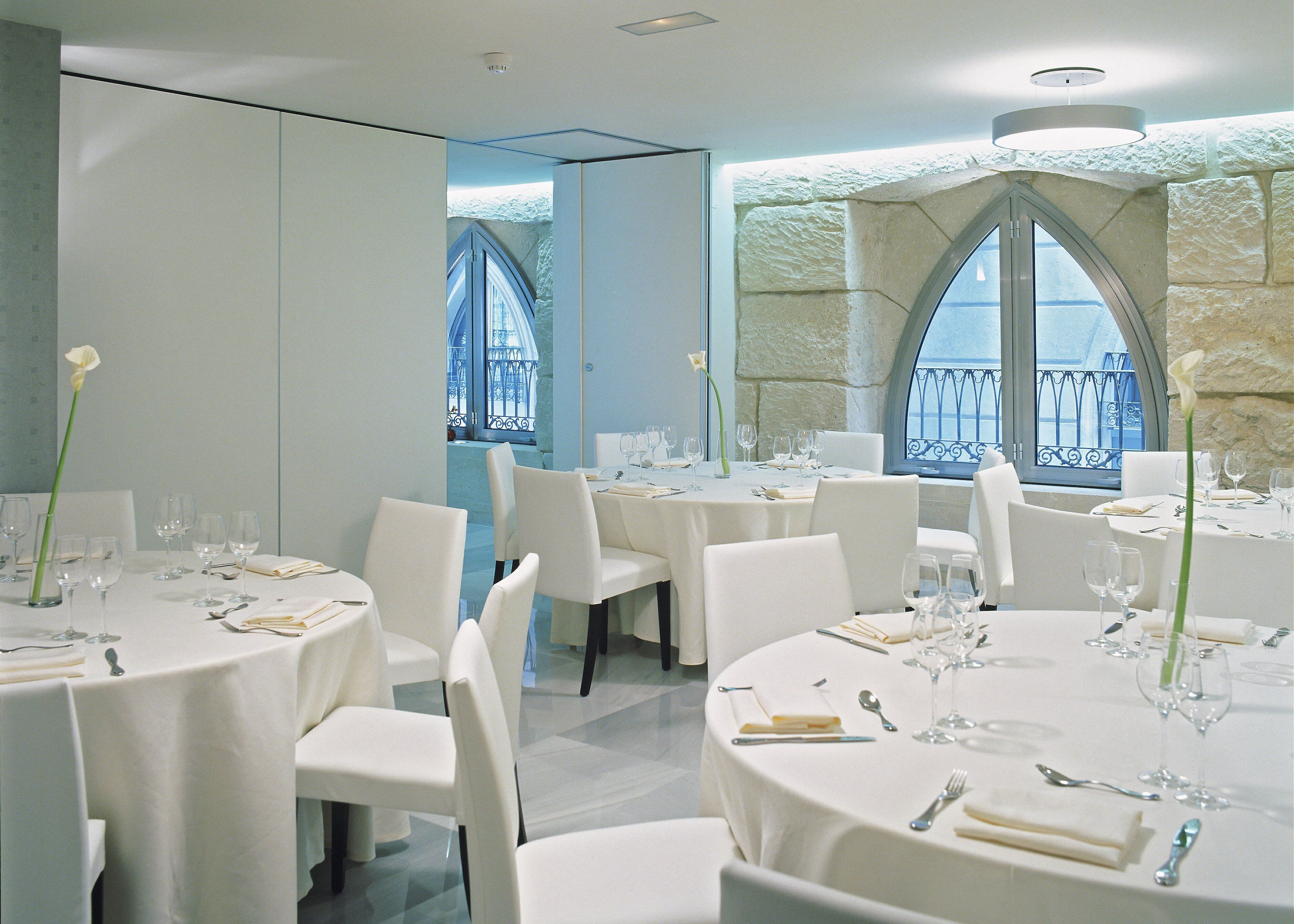 Un restaurant avec des tables rondes, des chaises blanches et un mur en pierre.