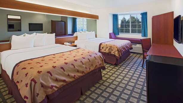 A hotel room with two beds, a TV, a desk, and a window with curtains. - Microtel Inn & Suites by Wyndham Holland (Holland)