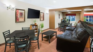 A hotel room with a dining area, a sofa, a TV, and a window with a red awning. - Microtel Inn & Suites by Wyndham Holland (Holland)
