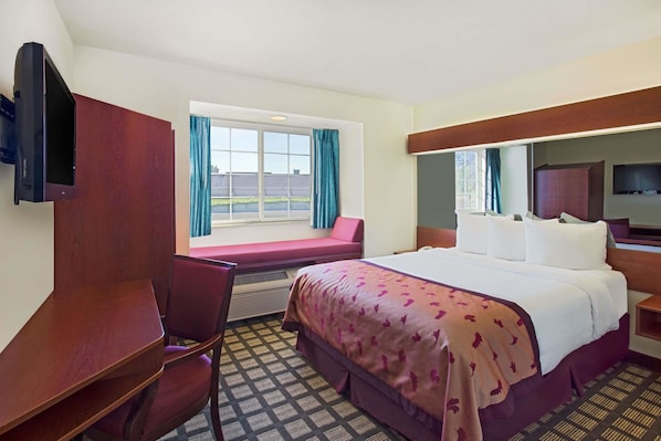 Ein Hotelzimmer mit Bett, Schreibtisch, Stuhl, Fernseher und einem Fenster mit Vorhängen.