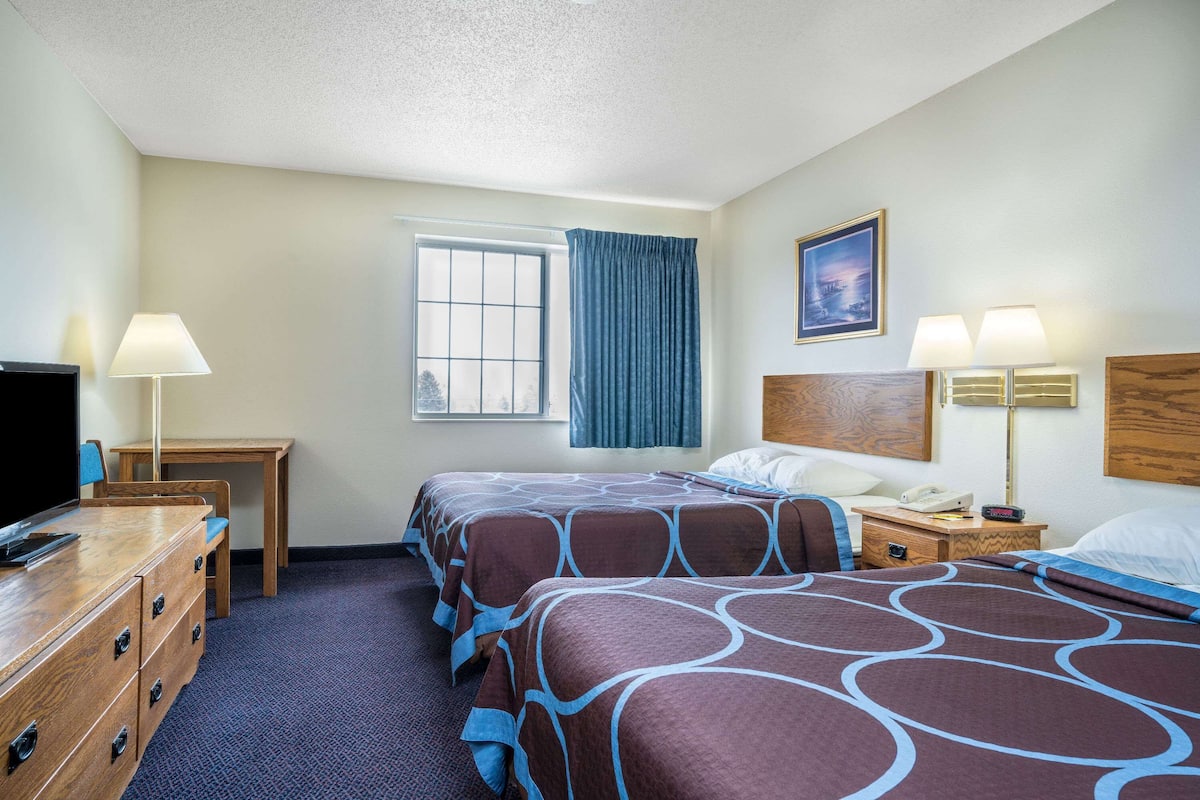 A hotel room with two beds, a desk, a TV, and a window with curtains.