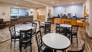 Een restaurantgedeelte in een hotel met ronde tafels en zwarte stoelen, een kitchenette met een koffieapparaat, en een bordje dat naar een zwembad en spa wijst.