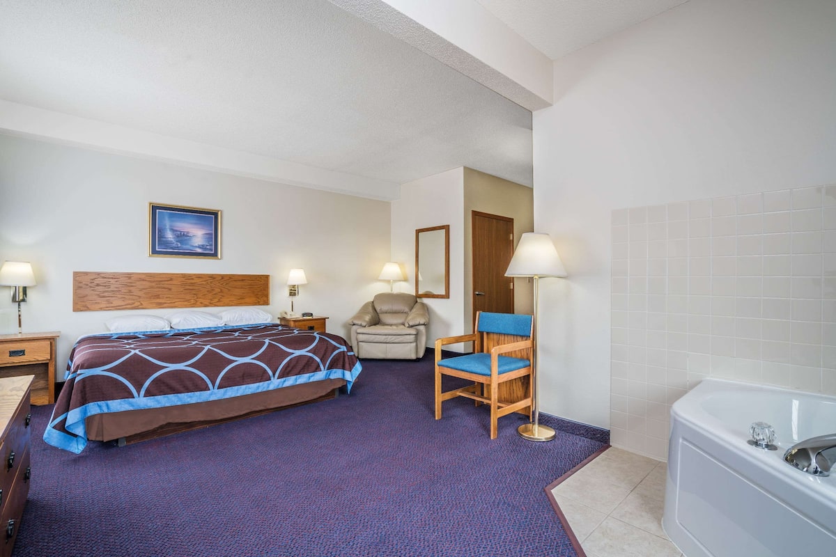 A hotel room with a bed, a chair, a desk, a lamp, a mirror, and a bathtub.