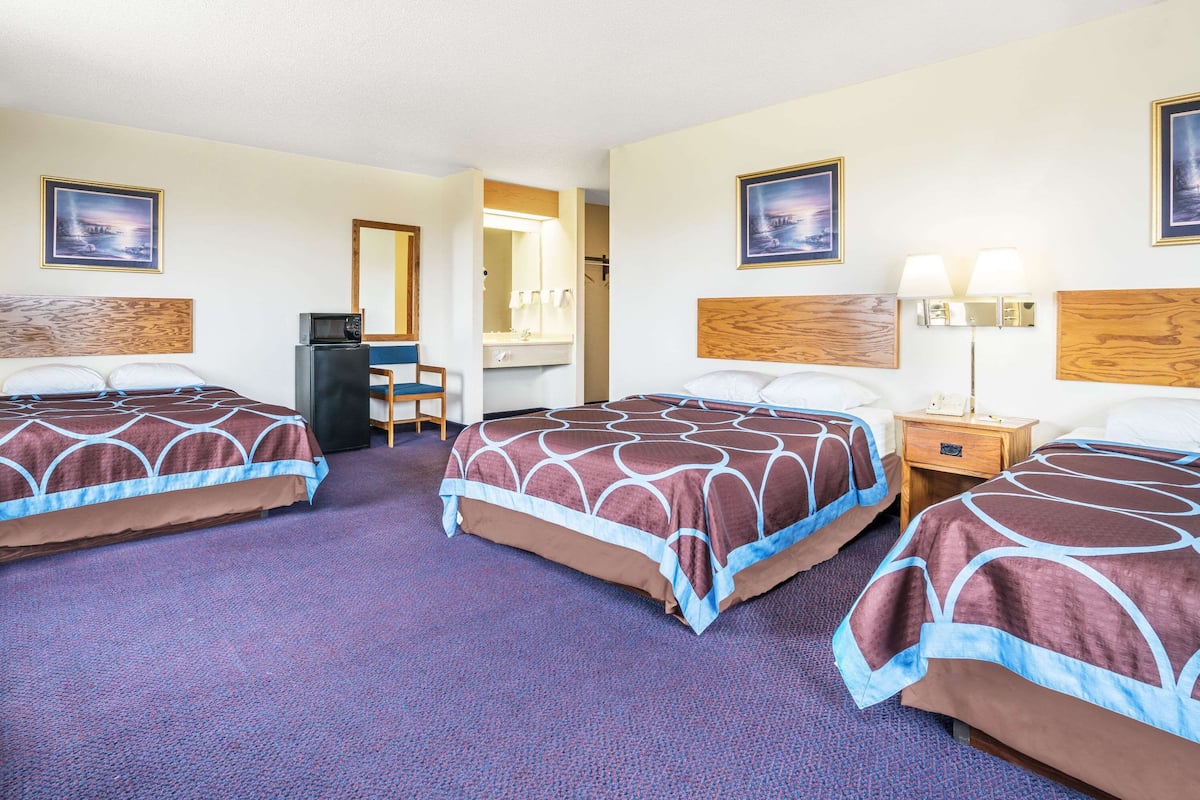 A hotel room with three beds, a desk, a chair, and a mirror.