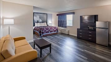 A hotel room with a bed, a sofa, a desk, a TV, and a refrigerator.