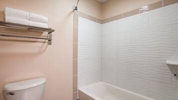 Un baño con inodoro, ducha con azulejos texturizados y toallero con toallas dobladas.