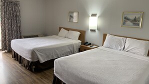 Et hotelværelse med to senge, et natbord med telefon og fjernbetjening, en væglampe og et vindue med gardiner.