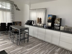 A modern kitchen with a dining area, featuring a coffee machine, a bread maker, and a kettle.