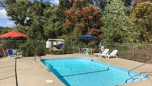 En rektangulær swimmingpool med en metalstige, omgivet af et hegn. Solstole og parasoller langs poolkanten.