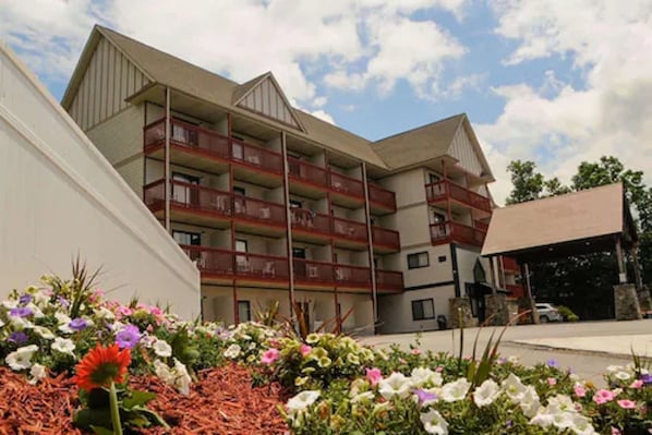 A multi-story building with balconies, surrounded by a garden with various flowers.