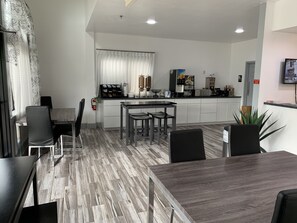 A modern kitchen with a dining area, featuring a central island, white cabinets, and a flat-screen TV mounted on the wall.