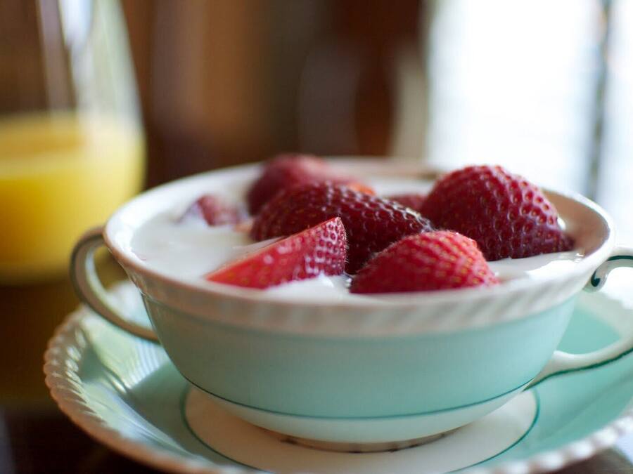 Un tazón de yogur con fresas sobre un platito azul claro.
