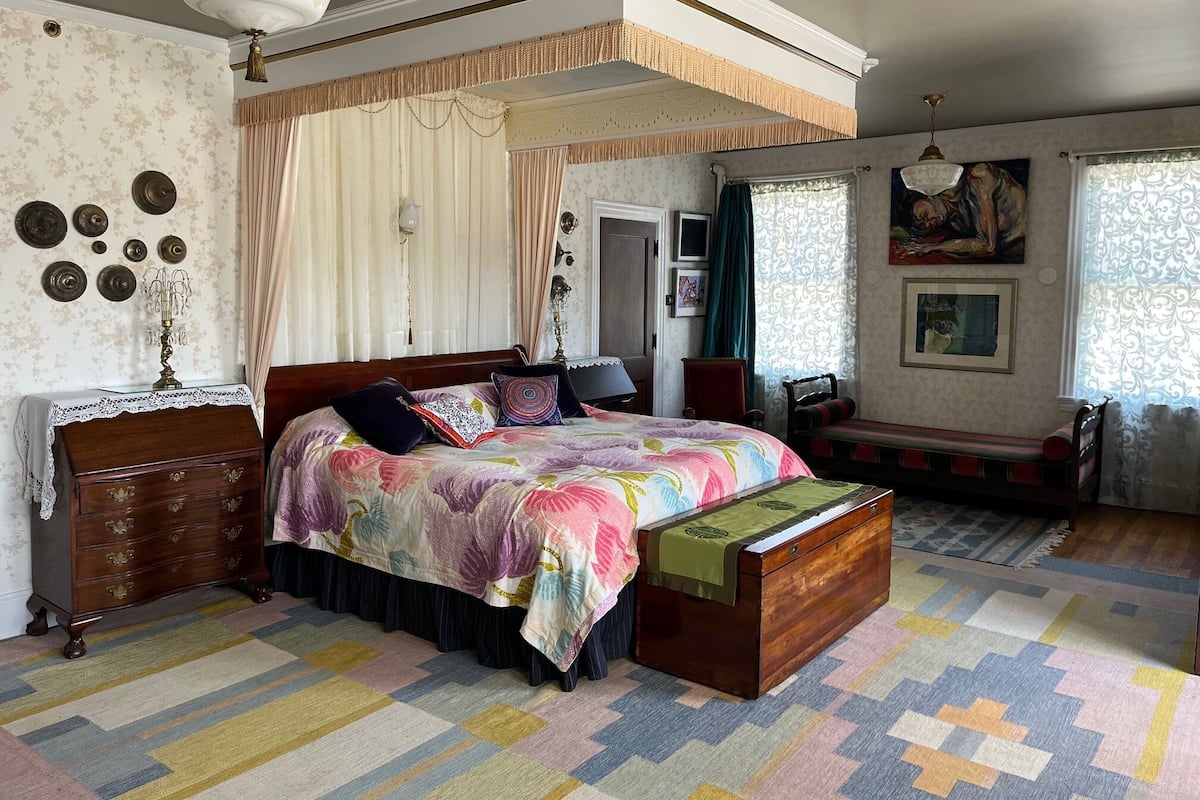 A bedroom with a large bed, a chest of drawers, a bench, and a ceiling fan.