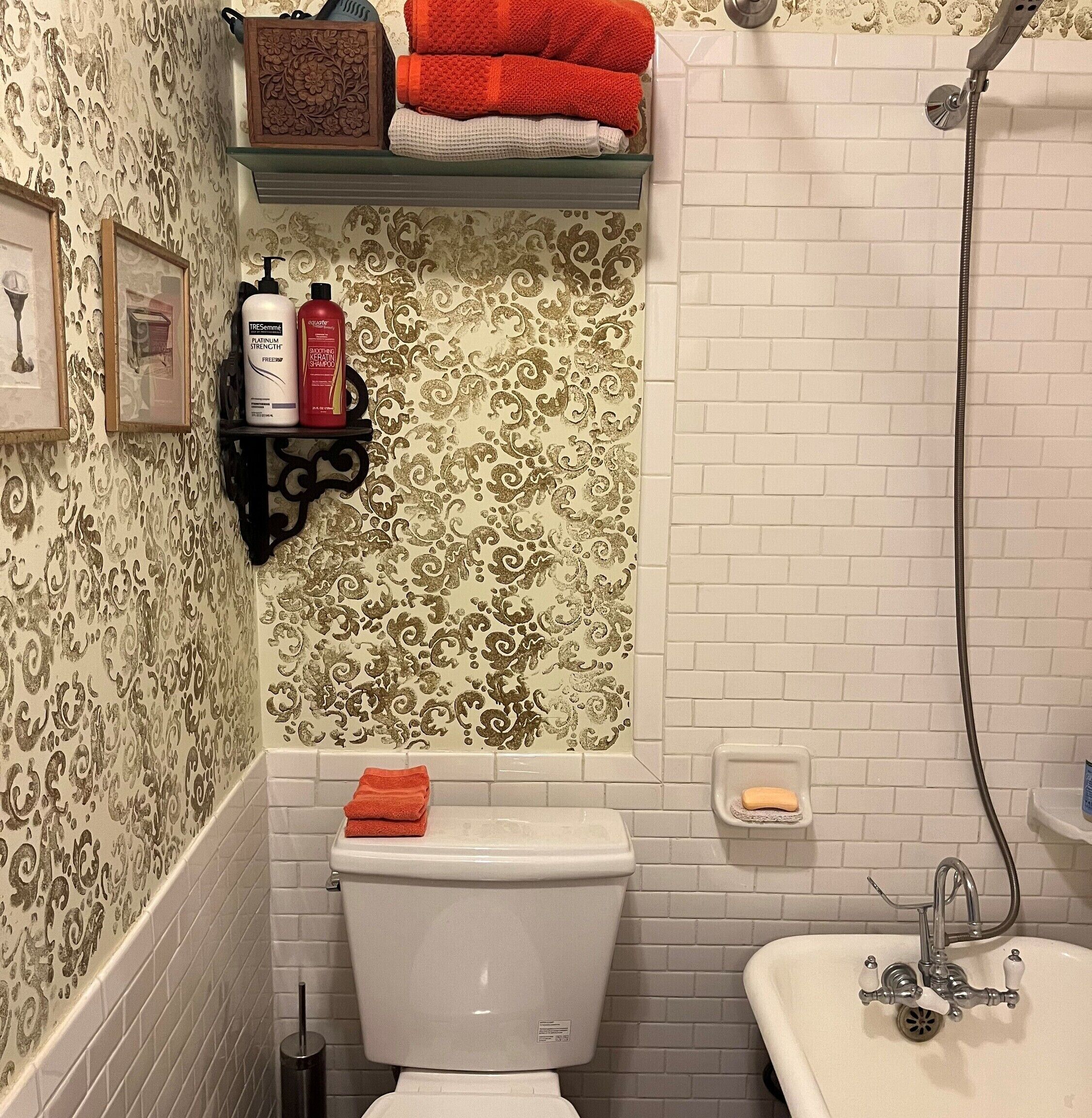 Een badkamer met behang met een patroon, een toilet, een douche en een plank met toiletartikelen.