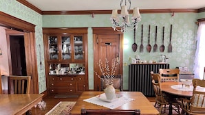 A dining room with a wooden table, chairs, a chandelier, and a cabinet with glass doors. - The Munroe Inn (Auburn)