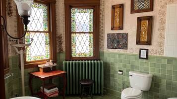 A bathroom with a green-tiled wall, a white toilet, a white sink, and a wooden vanity.
