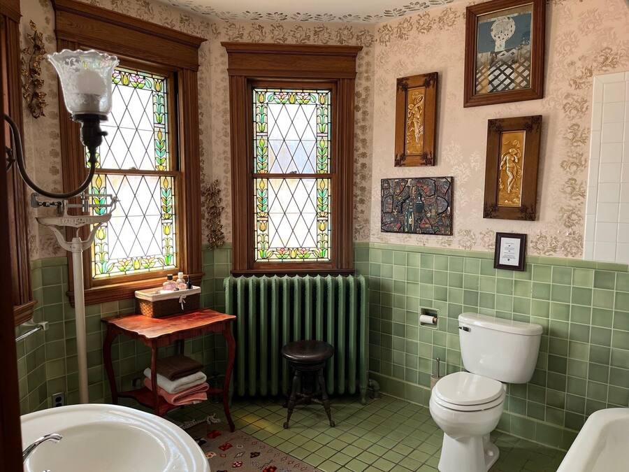 A bathroom with a green-tiled wall, a white toilet, a white sink, and a wooden vanity.