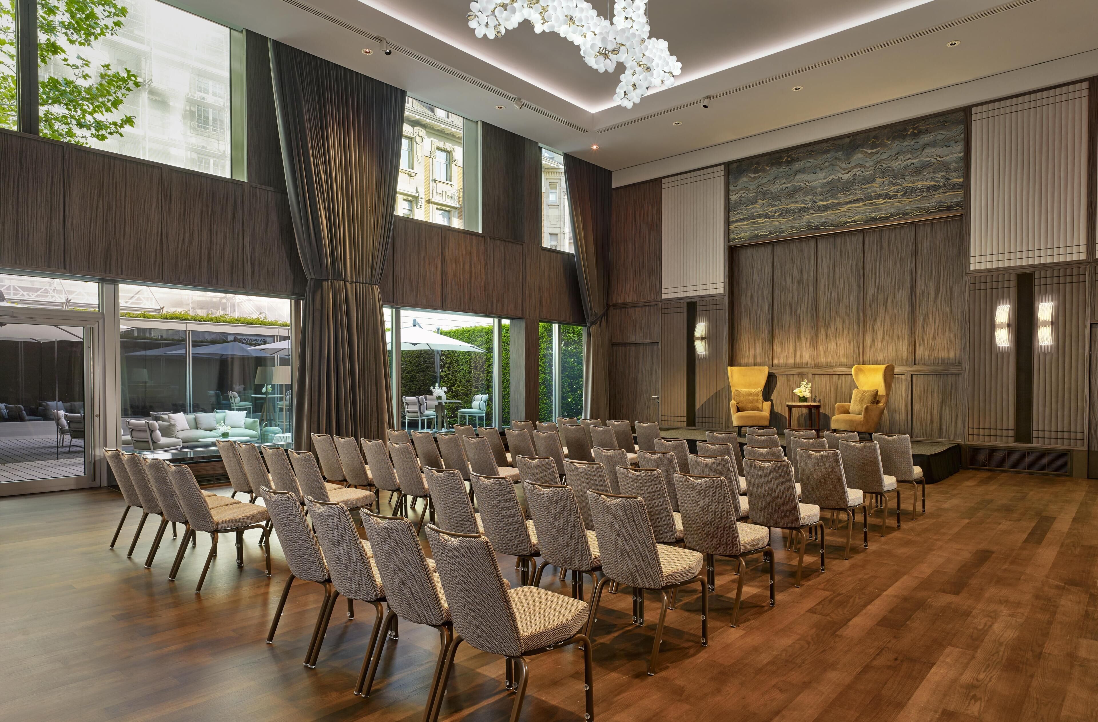 A conference room with rows of chairs, large windows, and a view of outdoor seating.