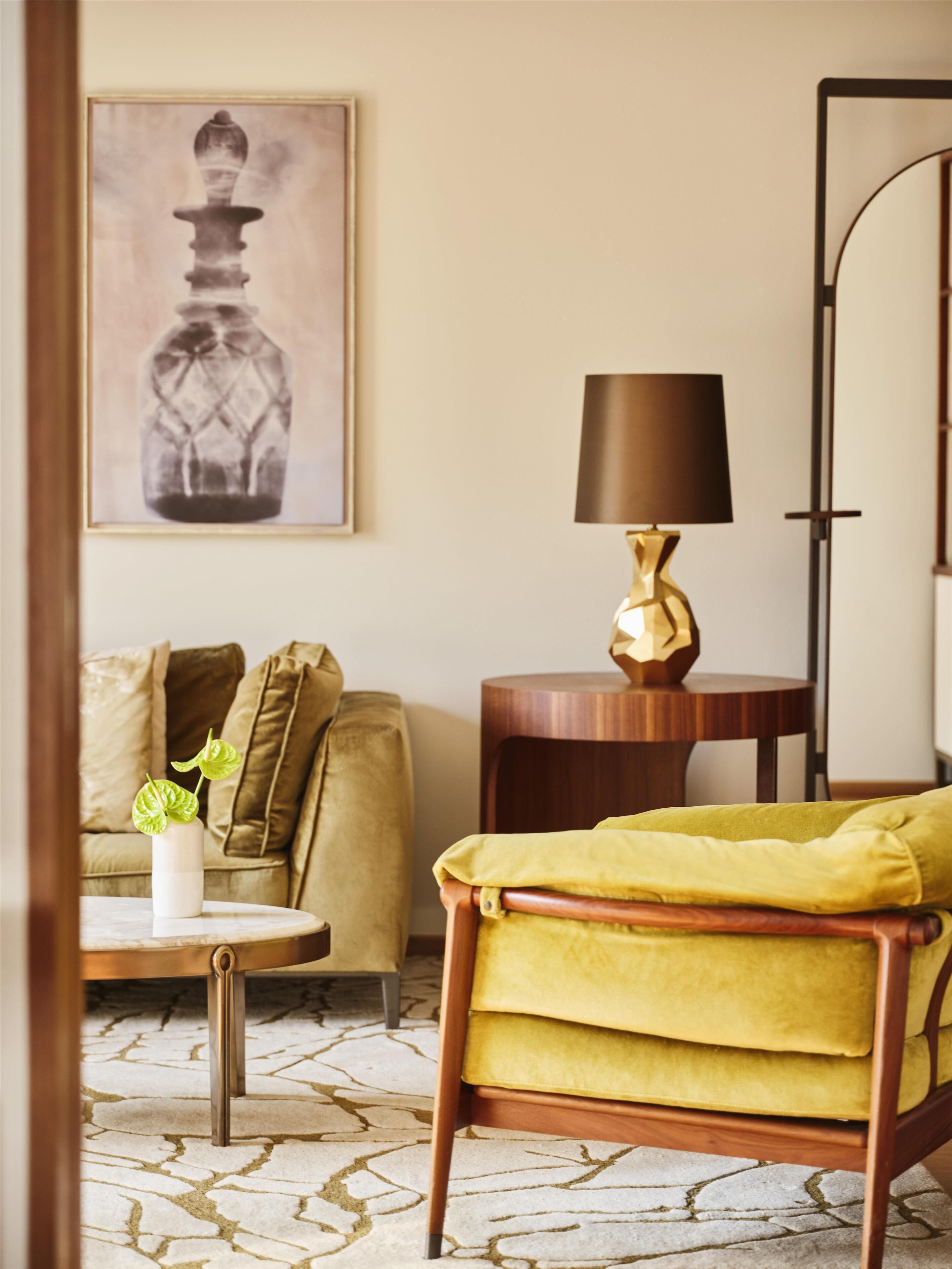 A room with a yellow armchair, a round coffee table, a lamp, a sofa, and a framed picture on the wall.