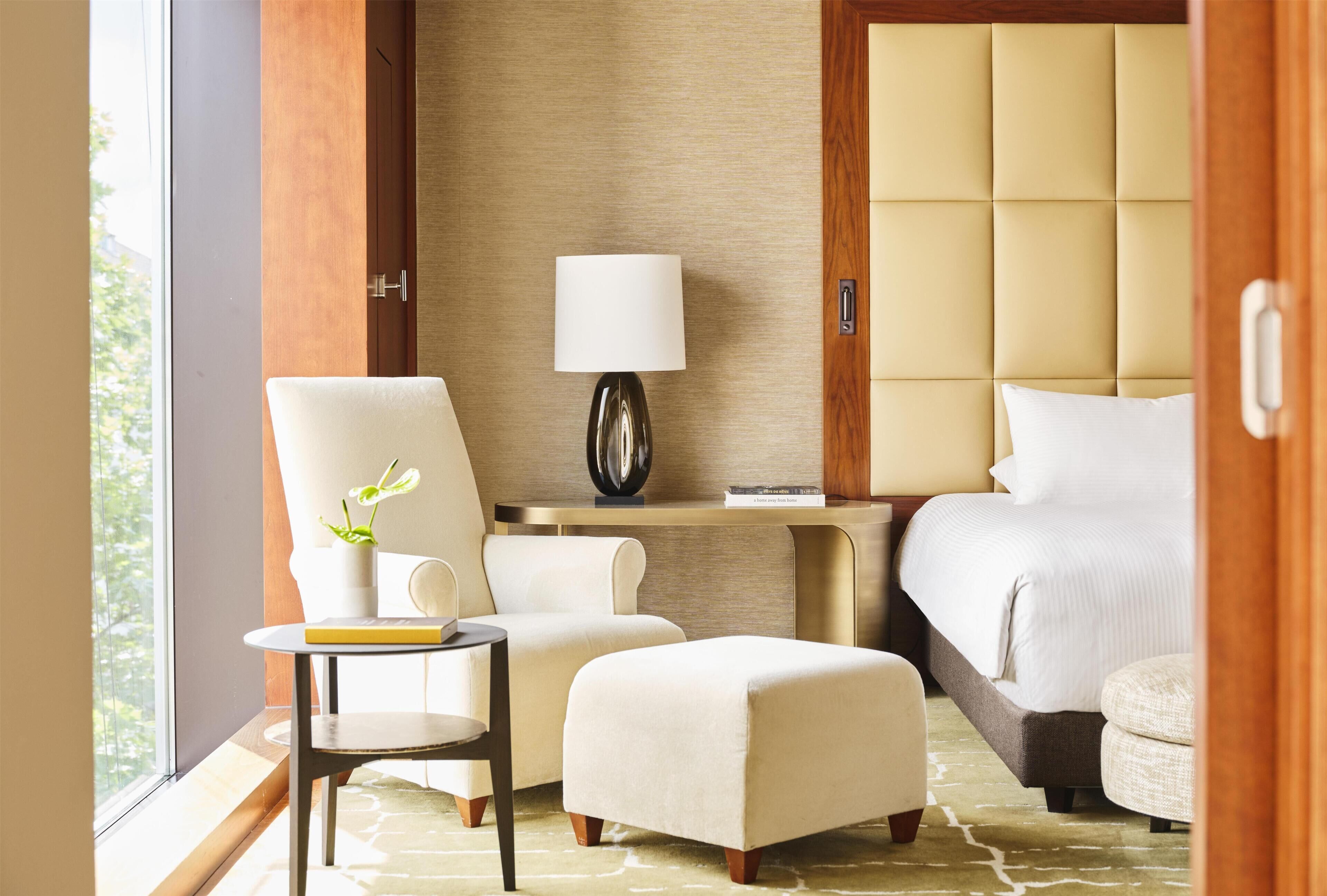 Habitación de hotel con cama, escritorio con lámpara, silla, mesita con planta y ventana.