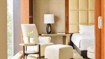 Habitación de hotel con cama, escritorio con lámpara, silla, mesita con planta y ventana.